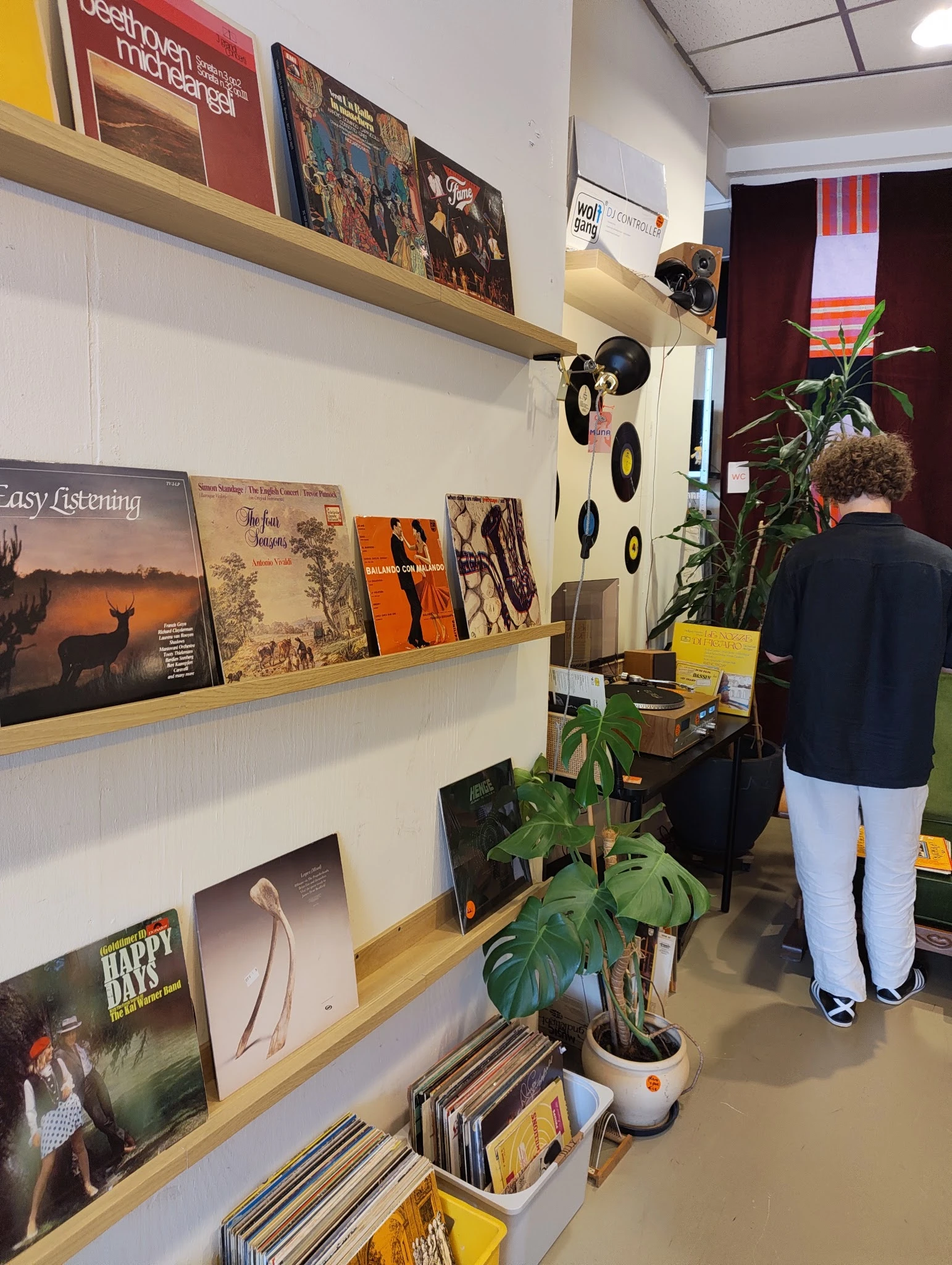 Wandrek met uitgestalde vinyl platen, boeken en decoratieve items in een kringloopwinkel