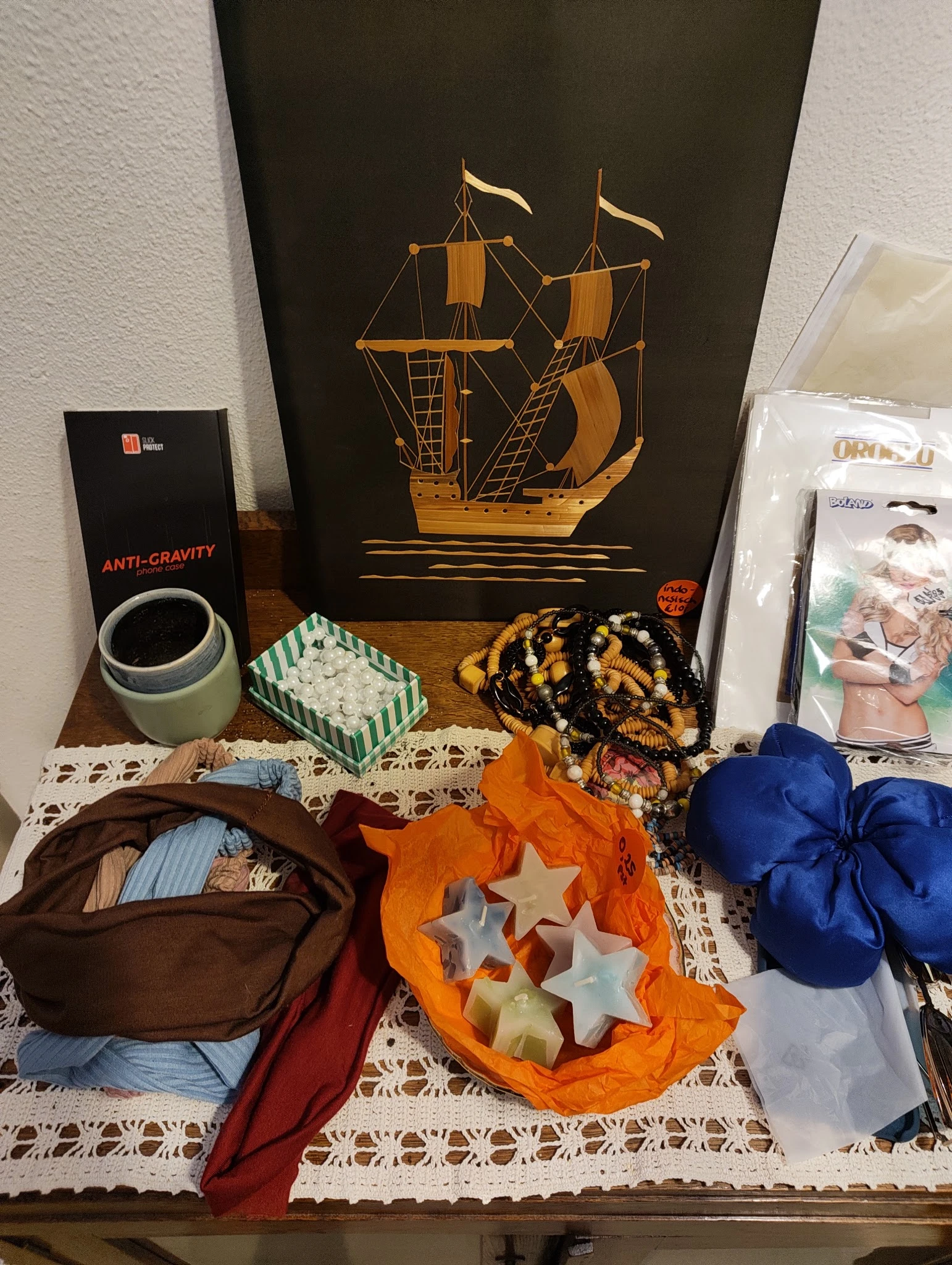 Verzameling tweedehands spullen op een tafel: anti-gravity pot, scheepsmodel, kleurrijke textiel en accessoires