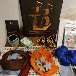 Verzameling tweedehands spullen op een tafel: anti-gravity pot, scheepsmodel, kleurrijke textiel en accessoires