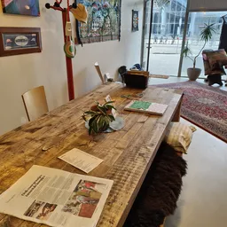 Houten tafel met stoelen, plant en papieren in een kringloopwinkel met zicht op de winkelruit en straat
