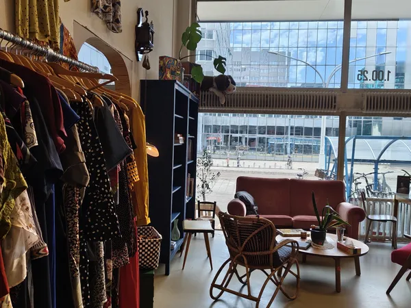 Winkelinterieur met kledingrekken links, zithoek met rode bank en stoelen in het midden, grote ramen met uitzicht op straat