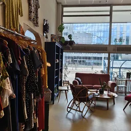 Winkelinterieur met kledingrekken links, zithoek met rode bank en stoelen in het midden, grote ramen met uitzicht op straat