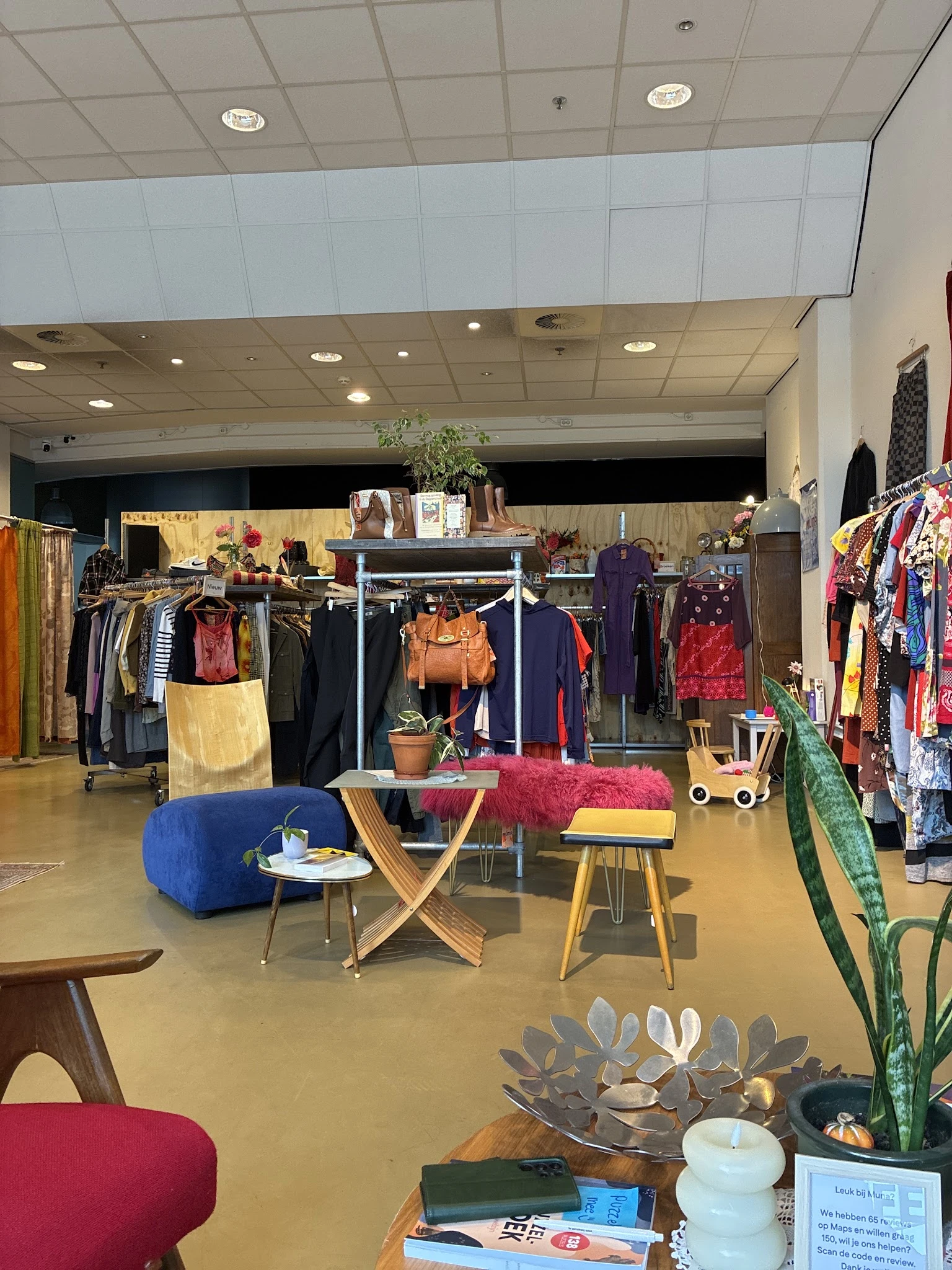 Winkelvloer met kledingrekken, vintage meubels en decoratieve items in een kringloopwinkel