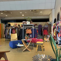 Winkelvloer met kledingrekken, vintage meubels en decoratieve items in een kringloopwinkel