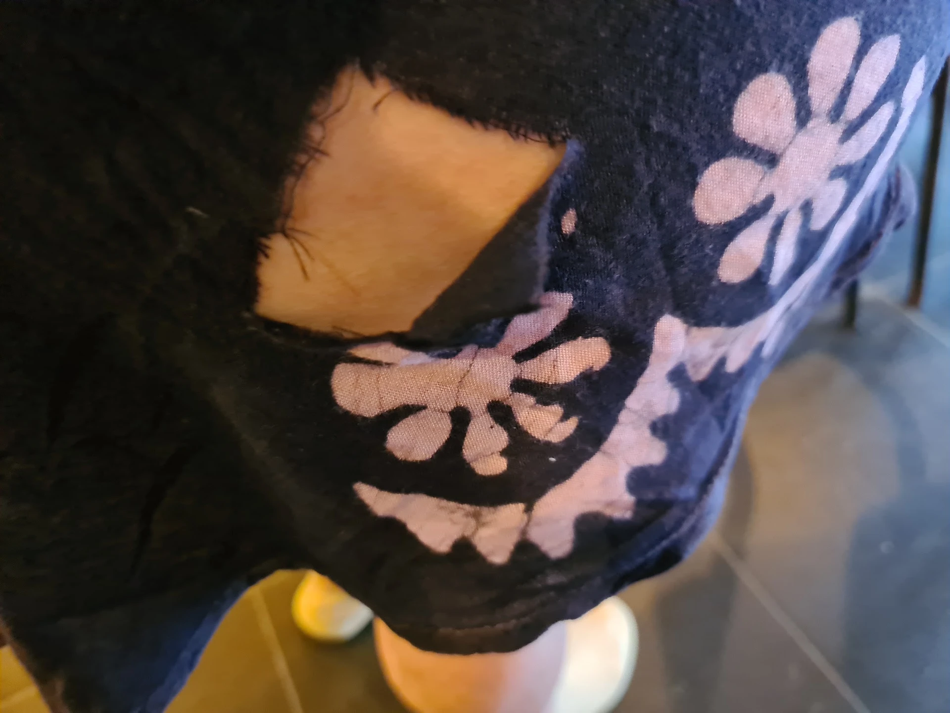 Close-up van een donkerblauwe trui of sweater met roze bloemenpatroon en een gat in de stof