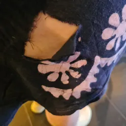Close-up van een donkerblauwe trui of sweater met roze bloemenpatroon en een gat in de stof