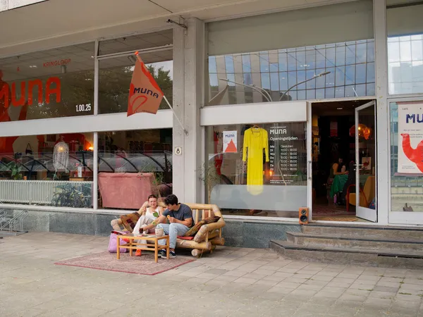 Winkelgevel met etalages en twee personen zittend op een houten bank op het terras ervoor