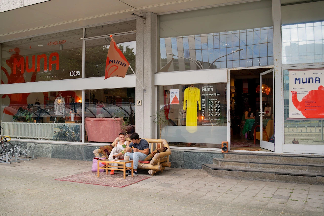 Winkelgevel met etalages en twee personen zittend op een houten bank op het terras ervoor