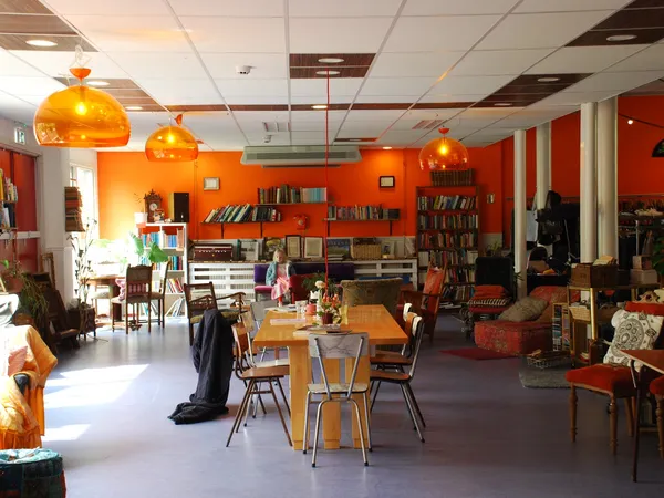 Winkelvloer met tafels, stoelen, boekenkasten tegen oranje wanden en gele hanglampen