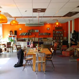 Winkelvloer met tafels, stoelen, boekenkasten tegen oranje wanden en gele hanglampen
