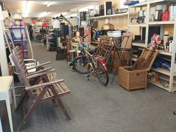 Winkelvloer met diverse tweedehands spullen: houten stoelen, fiets, rieten manden, stellingen met huishoudartikelen