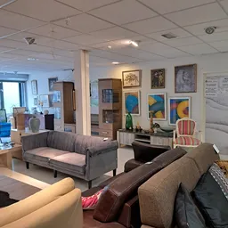 Woonkamer inrichting met zitmeubels, kunstwerken aan de muur en decoratieve voorwerpen in kringloopwinkel