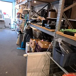 Rommelige winkelruimte met stellingen vol kartonnen dozen, kratten en diverse spullen