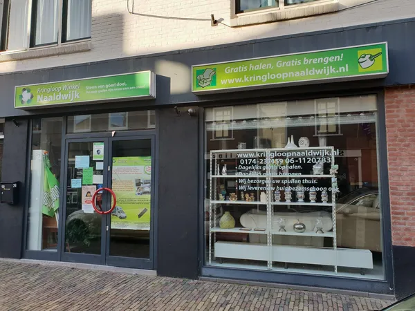 Gevel van kringloopwinkel met groene en zwarte uitstraling, glazen deur en etalageruit met huishoudelijke spullen