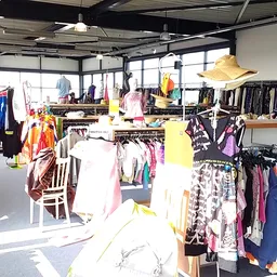 Winkelvloer van kringloopwinkel met rekken vol tweedehands kleding, veel daglicht via grote ramen