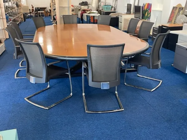 Grote ovale houten tafel met grijze stoelen op blauwe vloer in kantoorruimte