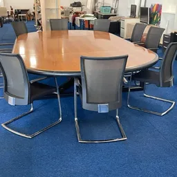 Grote ovale houten tafel met grijze stoelen op blauwe vloer in kantoorruimte