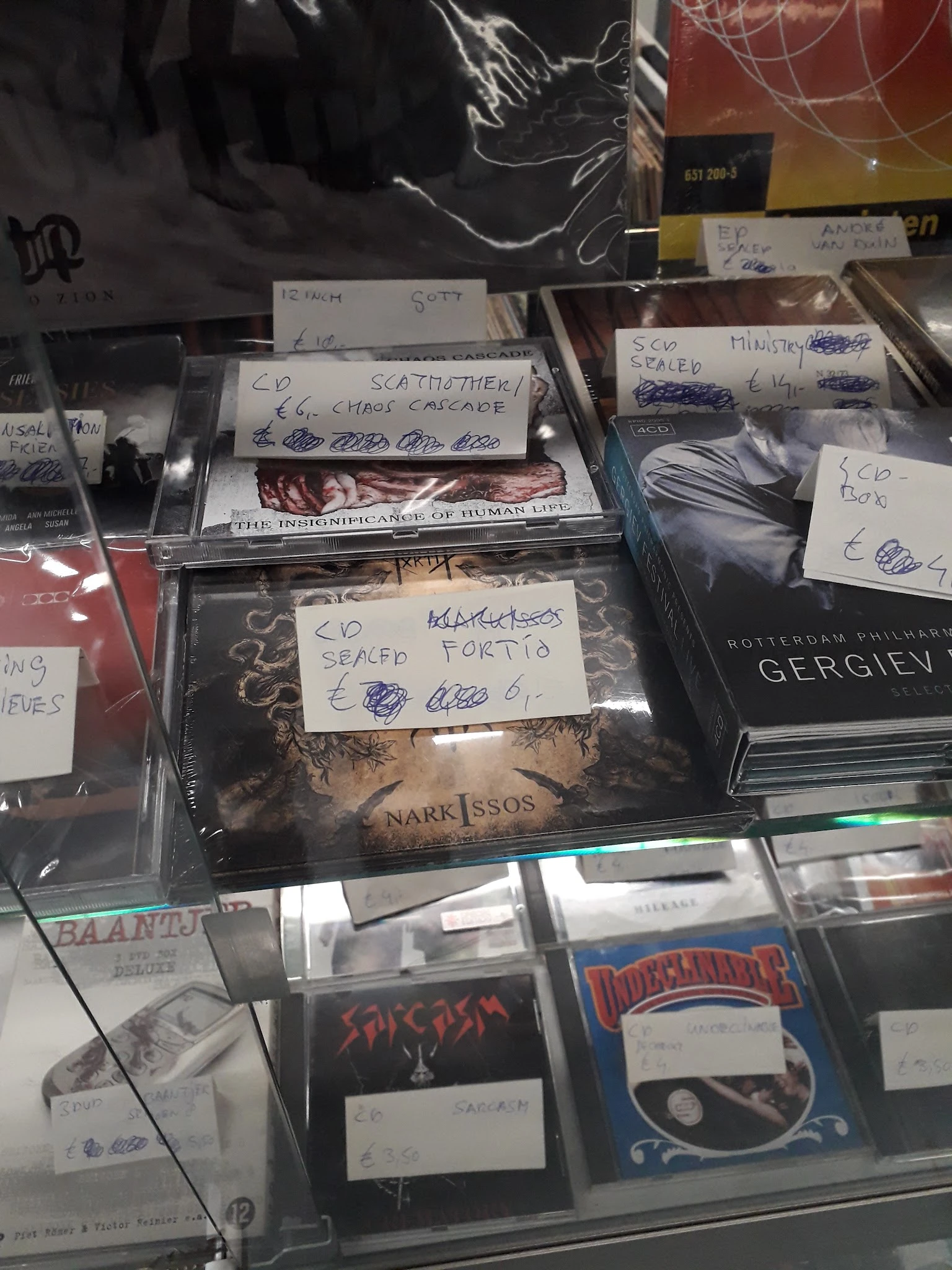 Diverse CD's en dvd's in plastic hoezen met handgeschreven prijskaartjes op kringloopwinkelplank
