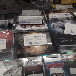 Diverse CD's en dvd's in plastic hoezen met handgeschreven prijskaartjes op kringloopwinkelplank