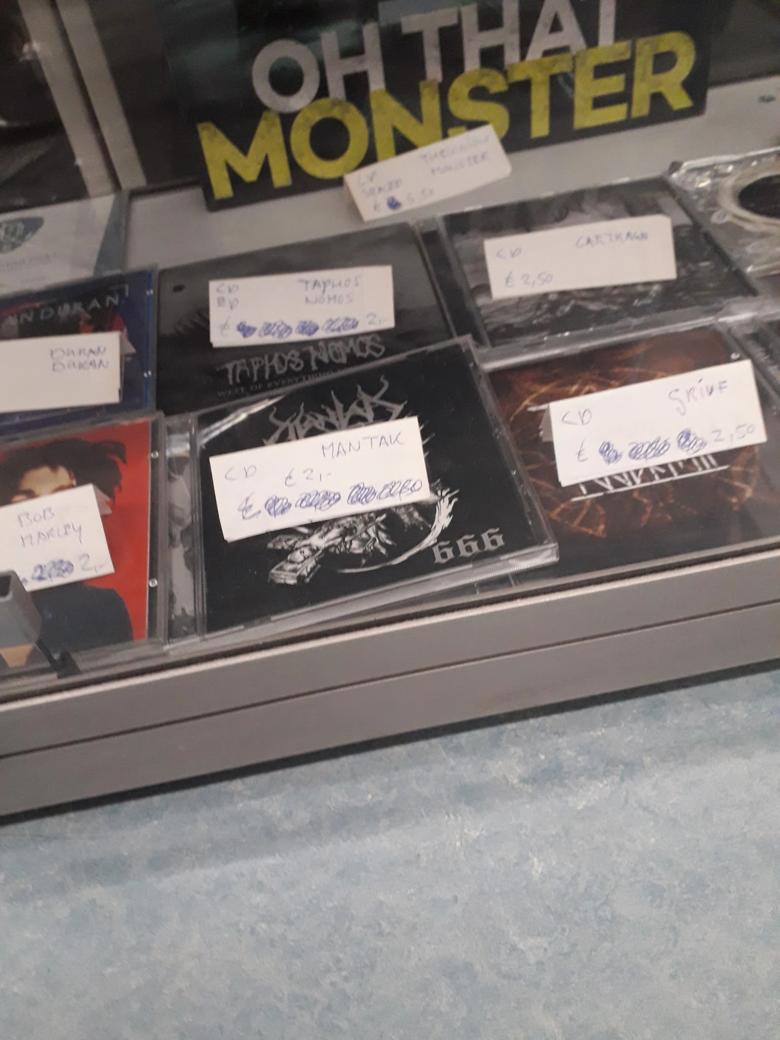 Uitgestalde cd's en dvd's in plastic hoezen met handgeschreven prijskaartjes in een winkelkast