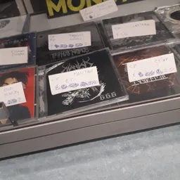 Uitgestalde cd's en dvd's in plastic hoezen met handgeschreven prijskaartjes in een winkelkast