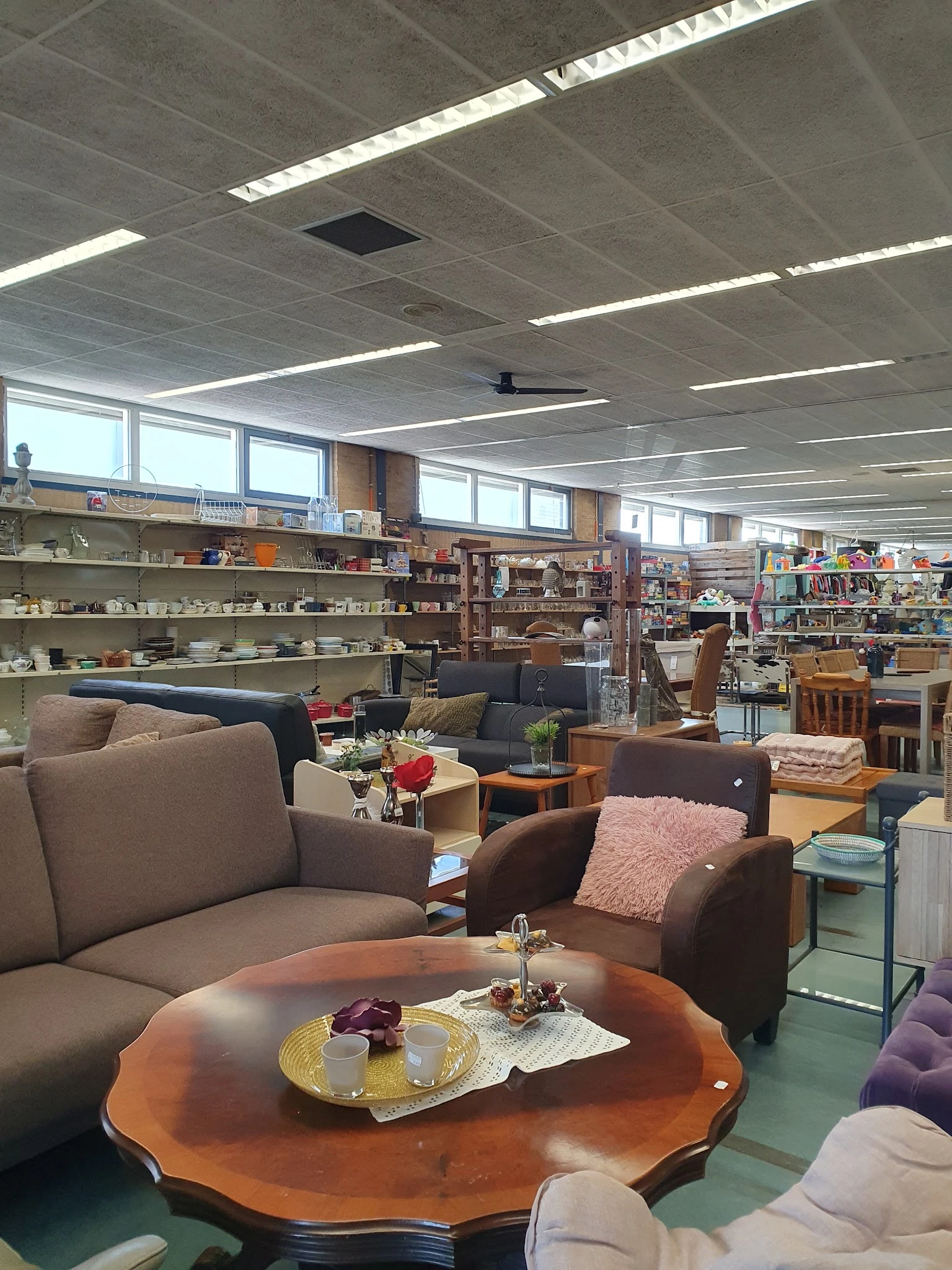 Zithoek met bruine fauteuils en banken, achtergrond met boekenrekken en huisraad in kringloopwinkel