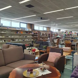 Zithoek met bruine fauteuils en banken, achtergrond met boekenrekken en huisraad in kringloopwinkel