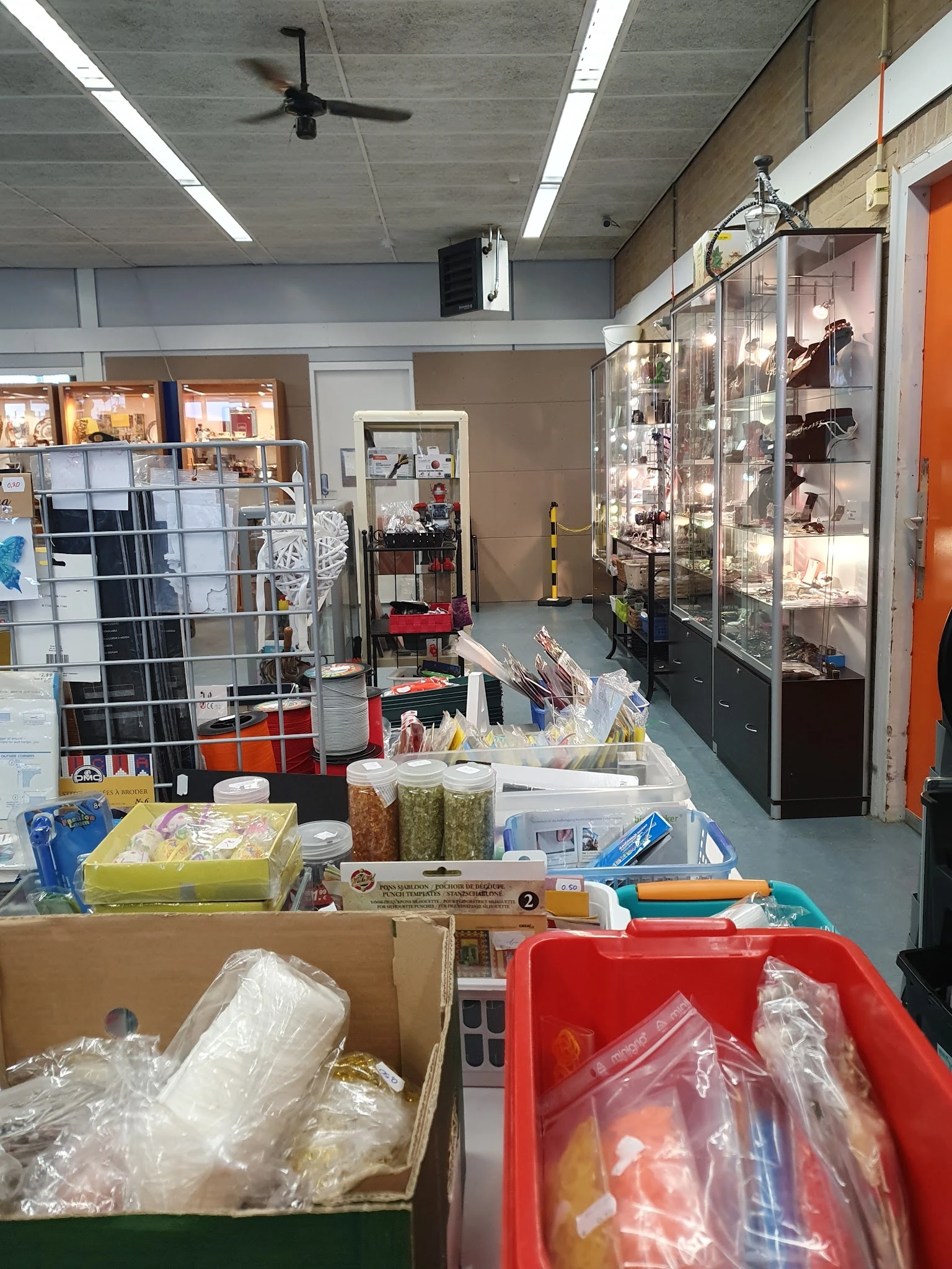 Winkelvloer van kringloopwinkel met diverse spullen, rekken, dozen en een glazen vitrinekast