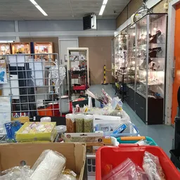 Winkelvloer van kringloopwinkel met diverse spullen, rekken, dozen en een glazen vitrinekast