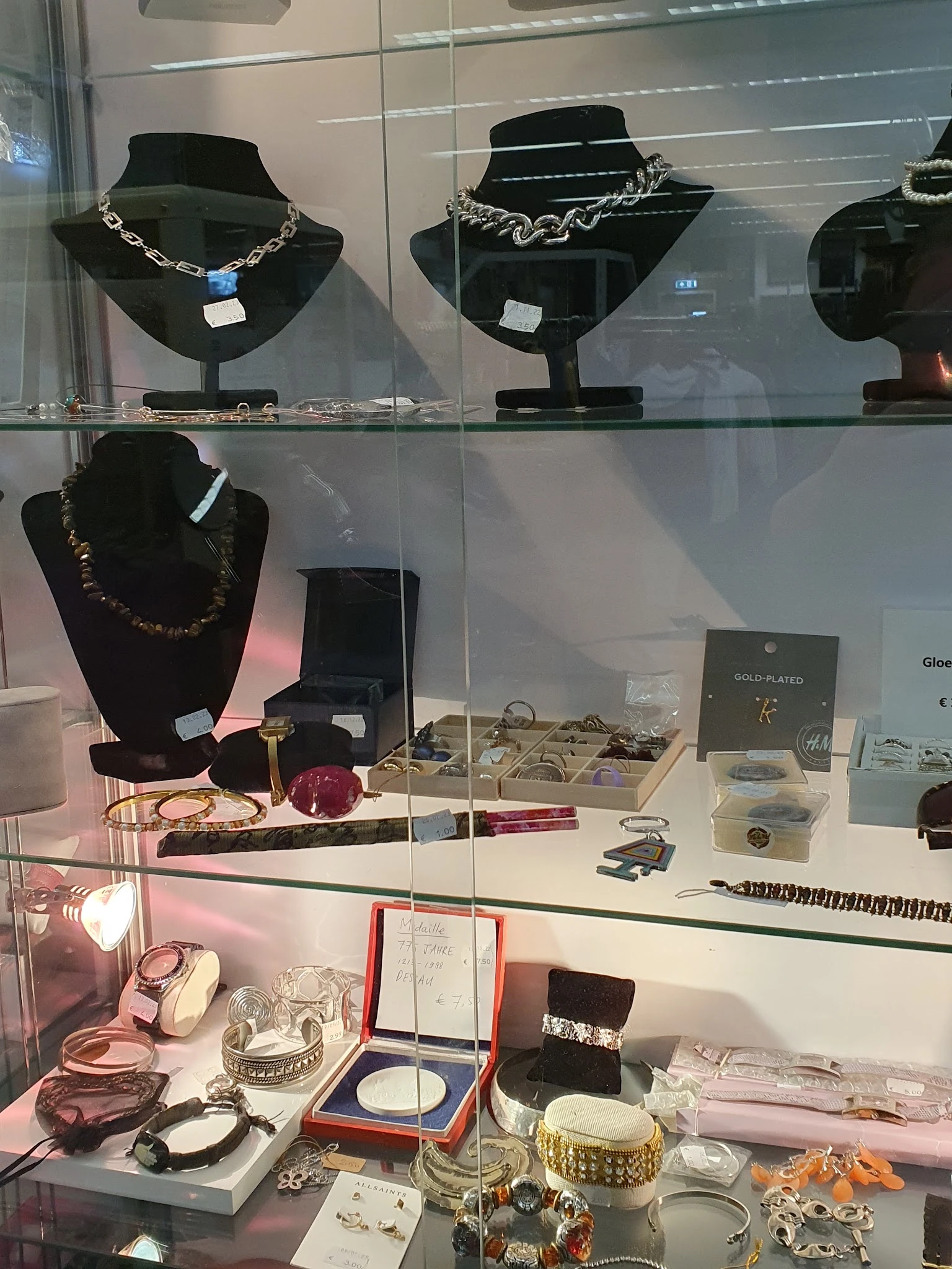 Glazen vitrine met sieraden, kettingen, ringen en accessoires uitgestald op wit oppervlak