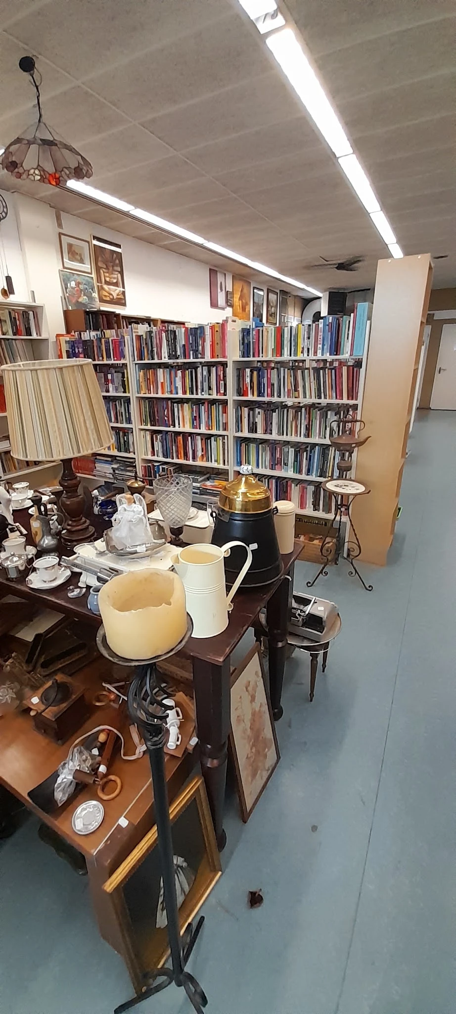 Binnenkant van kringloopwinkel met boekenkasten, tafel met serviesgoed en decoratieve objecten