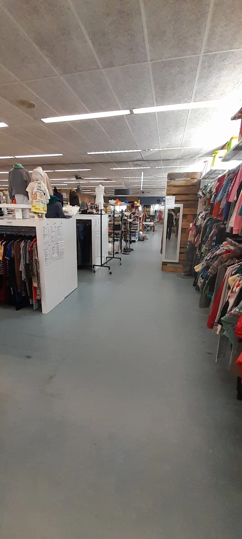 Winkelvloer met kledingrekken, stellingen en witte display-units in een kringloopwinkel