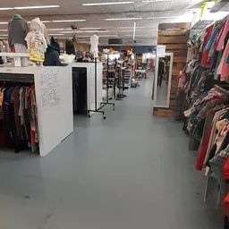 Winkelvloer met kledingrekken, stellingen en witte display-units in een kringloopwinkel