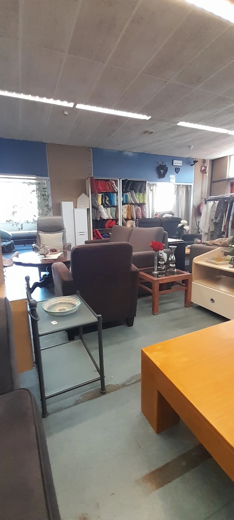 Winkelbinnenruimte met bruine fauteuils, kasten met kleding, tafels en natuurlijk licht van buiten