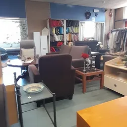 Winkelbinnenruimte met bruine fauteuils, kasten met kleding, tafels en natuurlijk licht van buiten