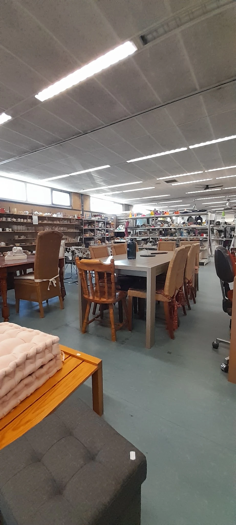Winkelvloer met eettafelset in het midden, stellingen en kasten vol spullen op de achtergrond, heldere verlichting