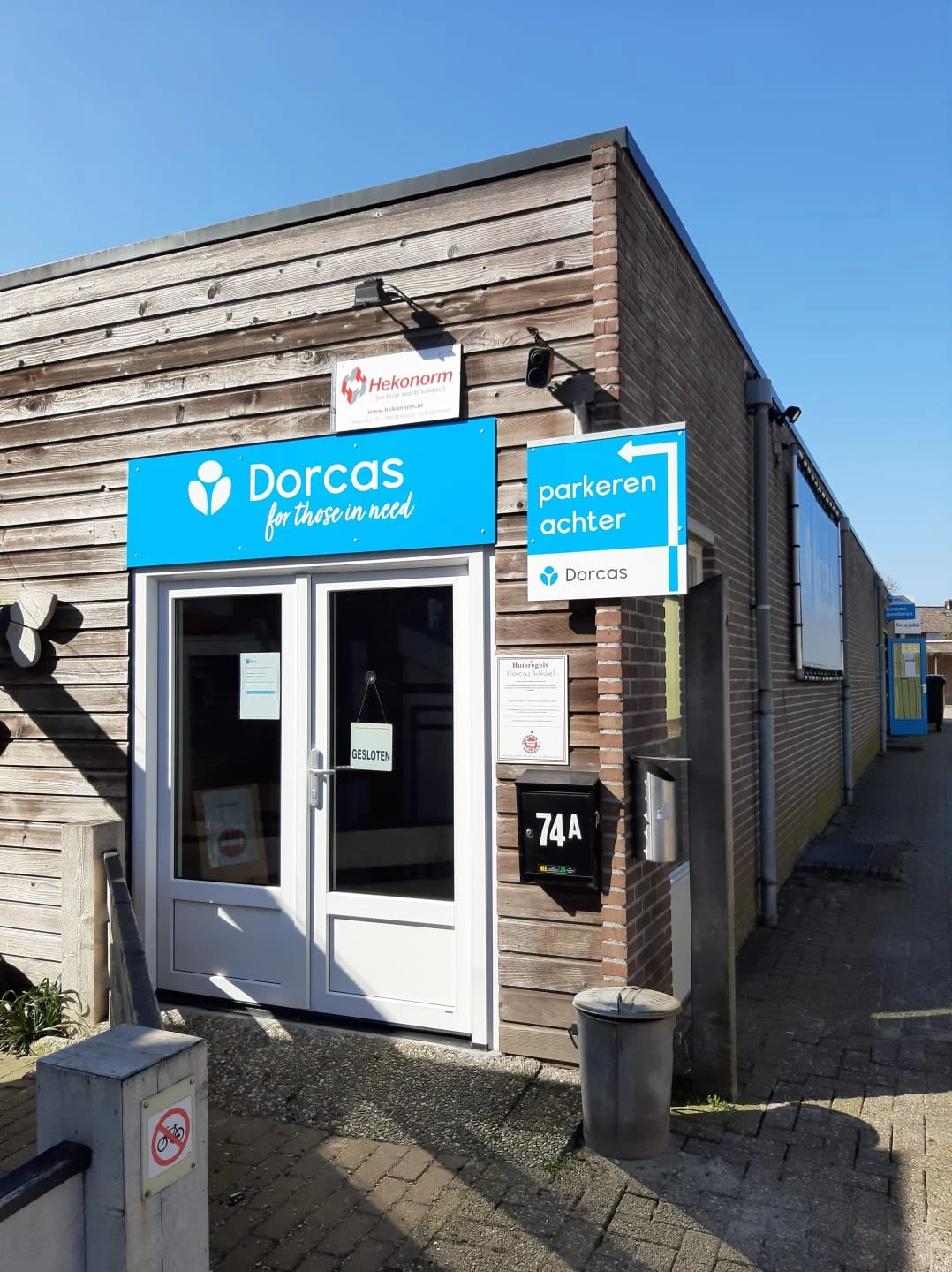 Voorgevel van kringloopwinkel met blauwe Dorcas-bord en parkeerachter-waarschuwingsbord