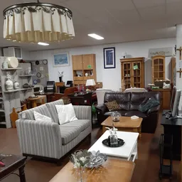 Woonkamer-opstelling met gestreepte fauteuil, zwarte leren bank, houten kasten en diverse meubels en decoratie-items
