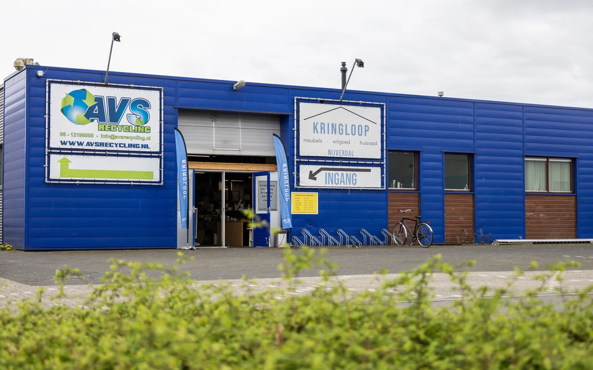 Blauwe gevel van kringloopwinkel met AVS-logo, ingang en signage aan de Nijverheidsweg