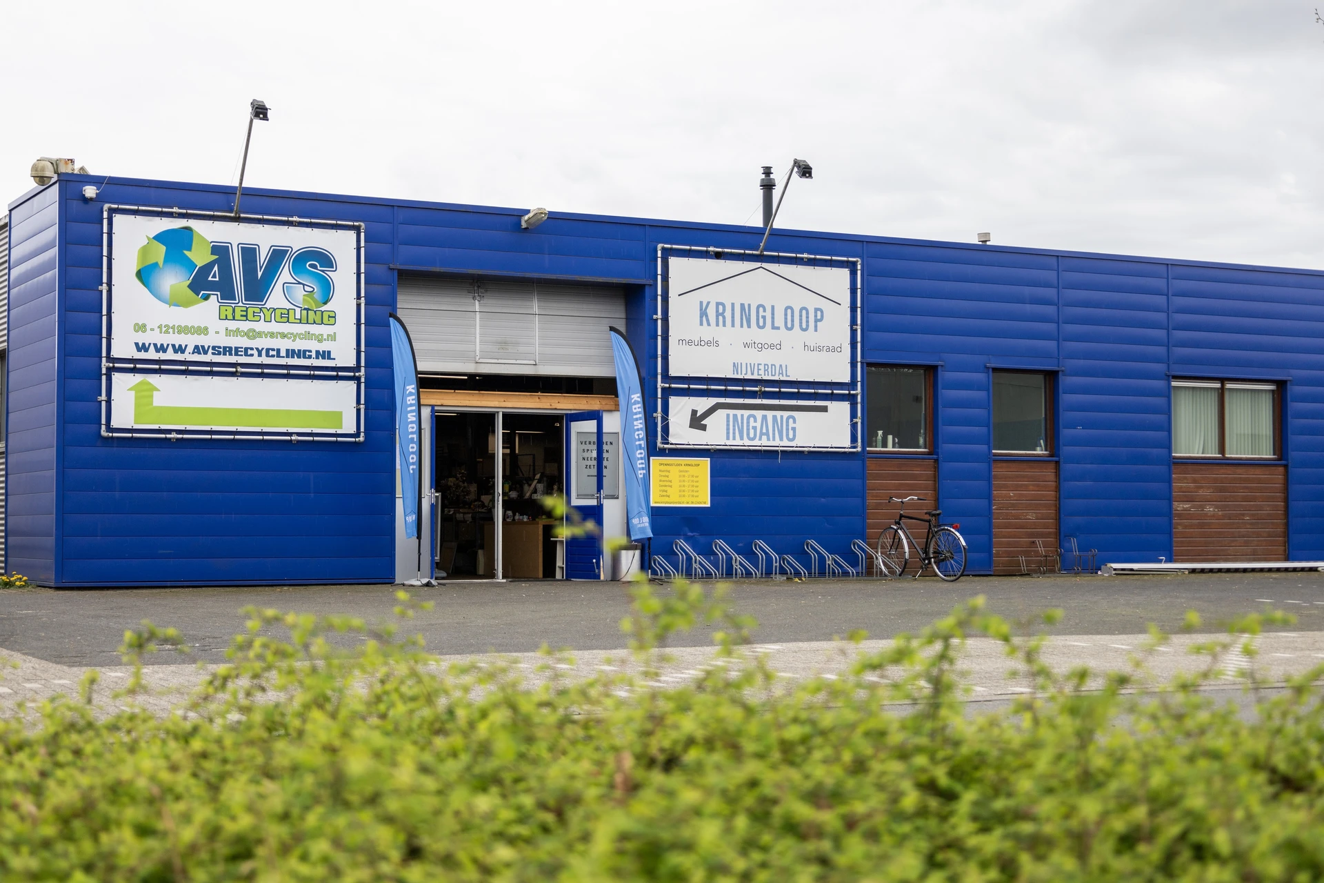 Blauwe gevel van kringloopwinkel met AVS-logo, ingang en signage aan de Nijverheidsweg