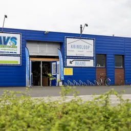Blauwe gevel van kringloopwinkel met AVS-logo, ingang en signage aan de Nijverheidsweg