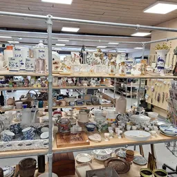 Uitgestalde serviesgoed, vazen, decoratieve items en huishoudelijke artikelen op planken en tafels in de winkel