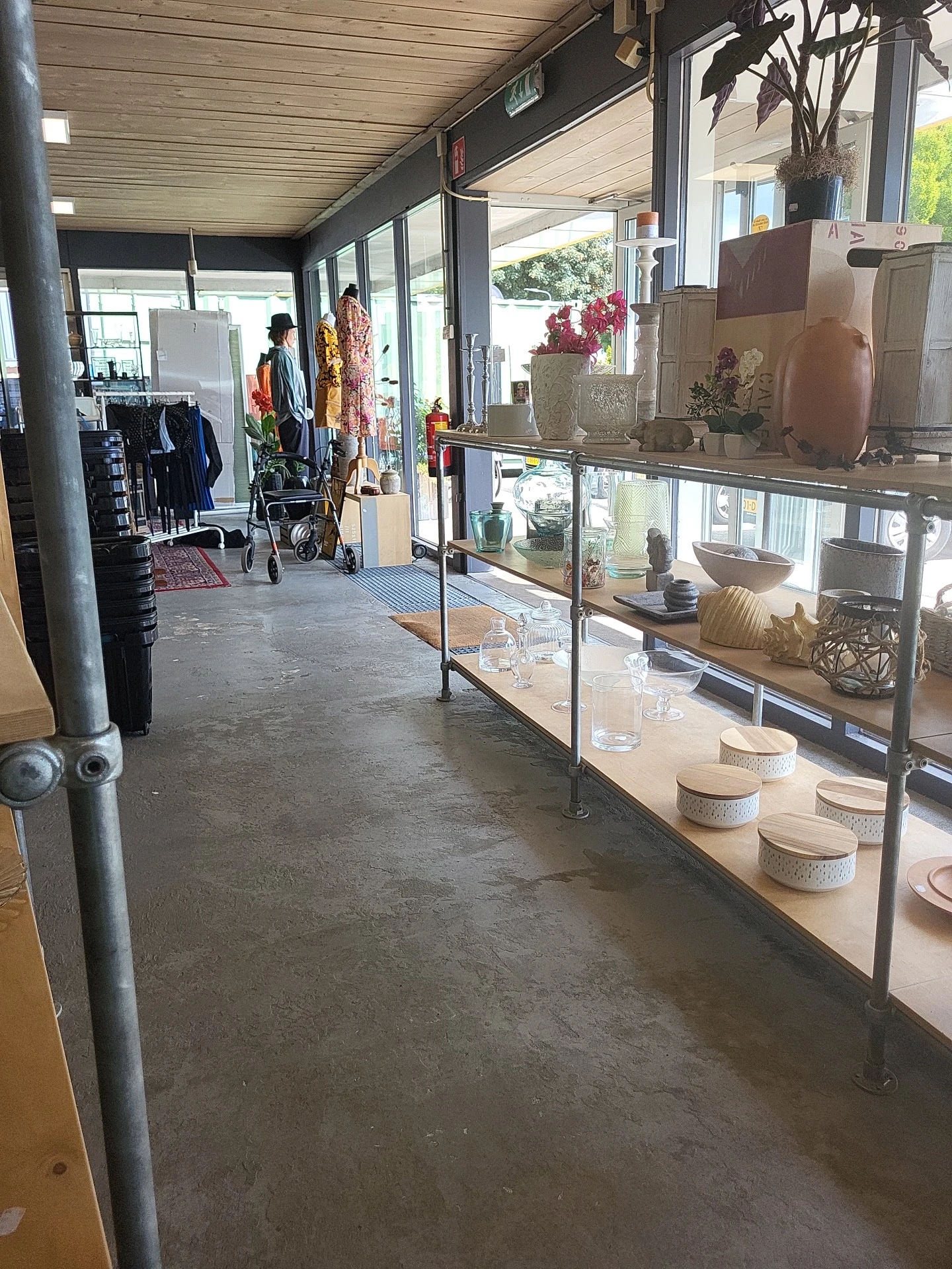 Winkelinterieur met glazen vitrine vol potten en decoratieve items, stellingen met kleding op achtergrond