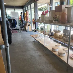 Winkelinterieur met glazen vitrine vol potten en decoratieve items, stellingen met kleding op achtergrond