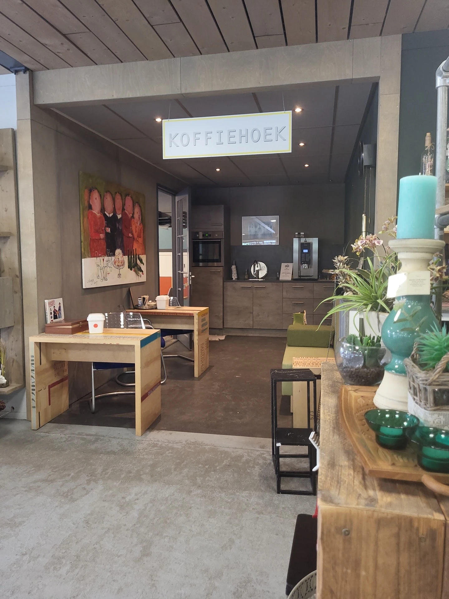 Winkelbinnenruimte met houten tafels, zwarte keuken, groen decor en rode kunstwerk aan de wand