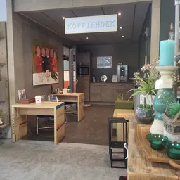 Winkelbinnenruimte met houten tafels, zwarte keuken, groen decor en rode kunstwerk aan de wand