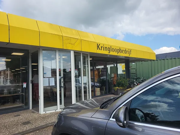 Gele gevel van kringloopwinkel met glazen deuren en winkelnaam boven de ingang