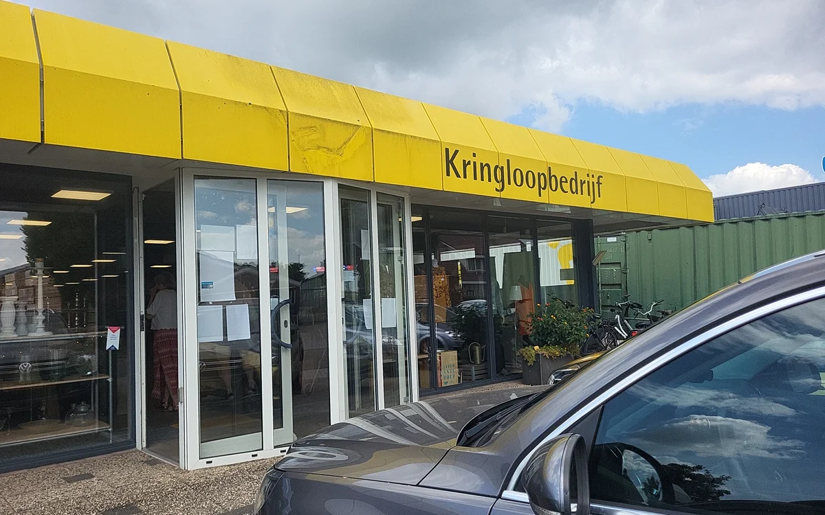 Gele gevel van kringloopwinkel met glazen deuren en winkelnaam boven de ingang