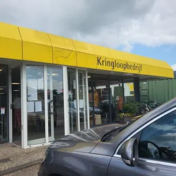 Gele gevel van kringloopwinkel met glazen deuren en winkelnaam boven de ingang