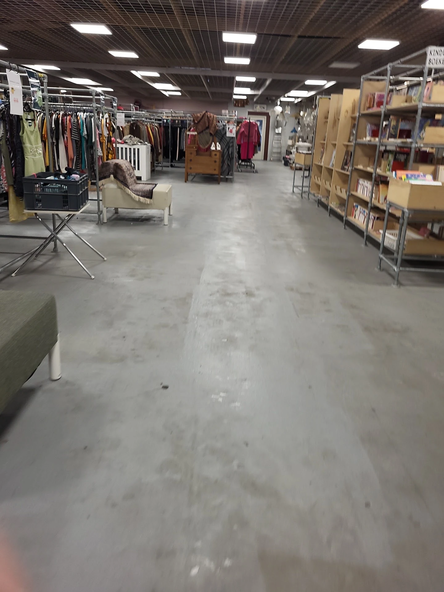 Winkelvloer van een kringloopwinkel met stellingen, kledingrekken en boekenkasten langs de zijkanten